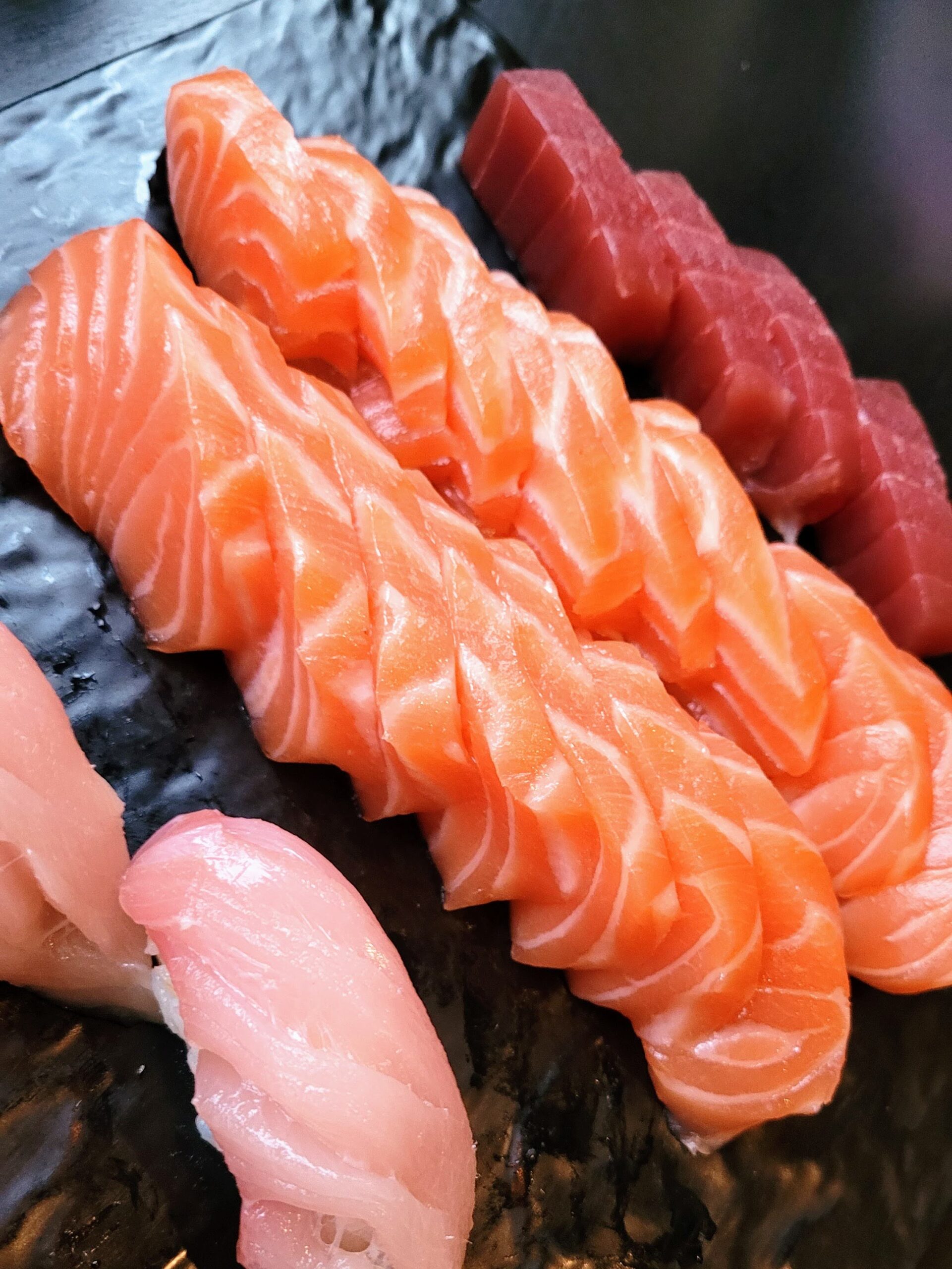 A close-up of assorted sushi sashimi, including salmon, tuna, and white fish, arranged on a dark surface.