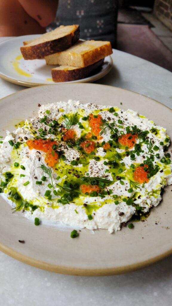 A plate of ricotta garnished with salmon roe, chopped chives, dill, black pepper, and olive oil - perfect for a mouth-watering foodie photo.