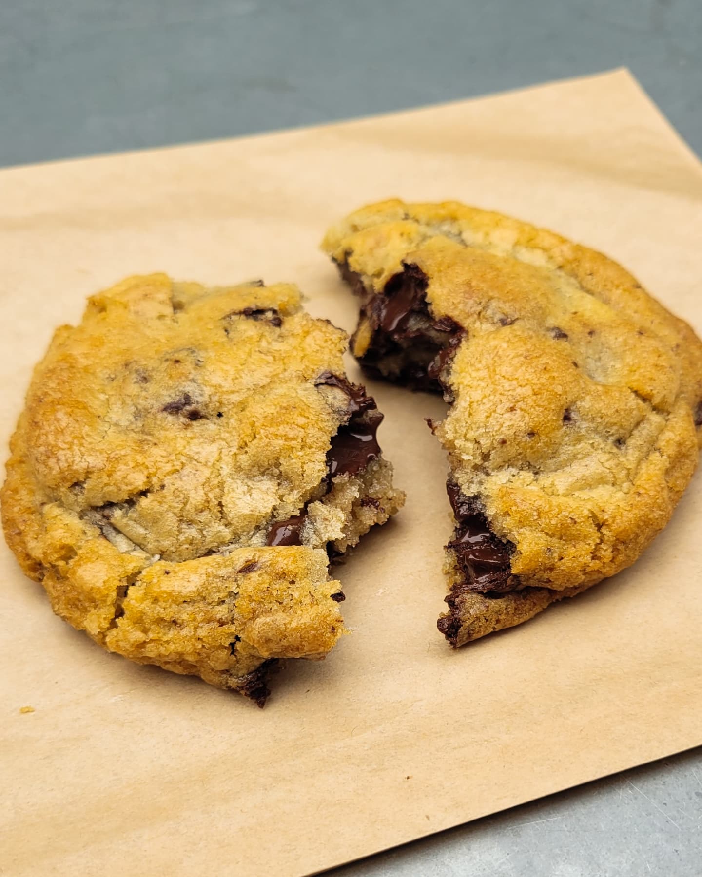 A chocolate chip cookie broken in half rests on a piece of brown parchment paper.