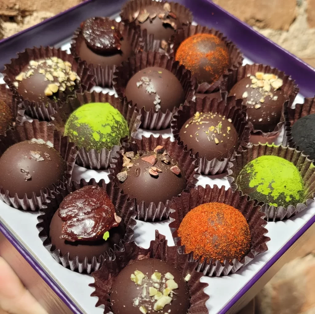 A box of assorted dark chocolate truffles in different flavors, including green tea, chili, dried fruit, and nuts.